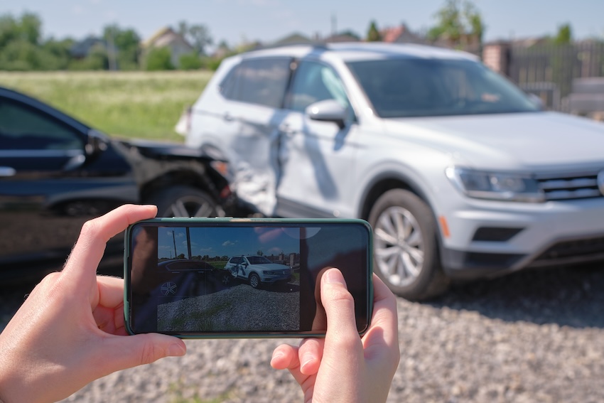 Person photographing vehicle damage and accident scene with smartphone to document evidence for Georgia insurance claim
