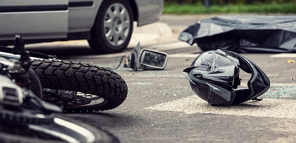 A scene of a motorcycle accident where a car hit a motorcyclist and now there are fallen vehicle parts on the ground.