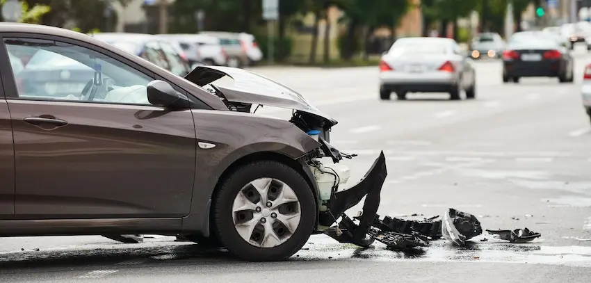 A brown sedan stopped on a busy city street with its entire front bumper and hood crumpled inward and debris scattered across the pavement representing the type of violent impact that frequently causes hidden injuries that victims may not feel until hours or days after the crash in Georgia.