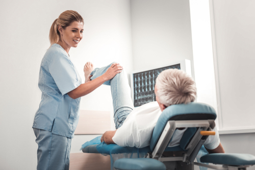 A female car accident chiropractor helping a man with a leg pain by stretching his leg in an office.
